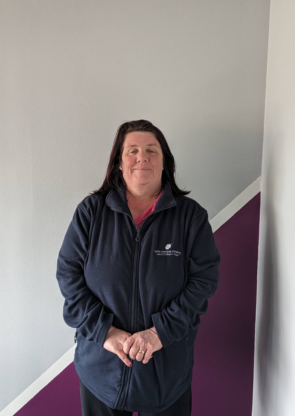 Image of Adrianne a women, with brown hair, wearing the ELI uniform pink shirt and blue jacket and smiling