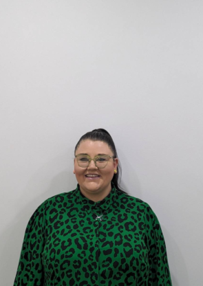 Smiling Amy with brown hair in a ponytail, light green glasses, and a darker green long sleeve top