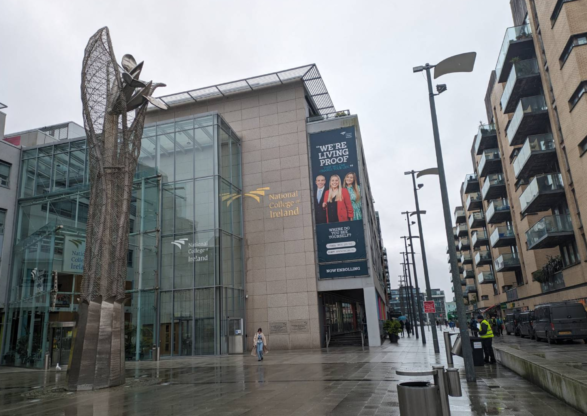 the outside of National College Ireland. With a glass entrance a large metal statue of growing flowers the height of the building