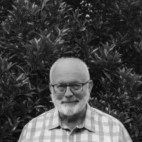 Smiling Edmond, a man with a short white beard and wearing glasses and plaid shirt