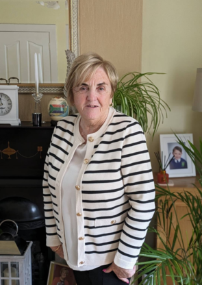 A smiling lady wearing a white Blazer with black stripes and gold buttons. She has light blonde hair and she's has a lovely smile and pink nails